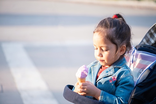 A little girl sitting in her pram, enjoying a strawberry ice-cream.