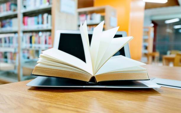 istock Laptop and open book on the table of public library 1193278099