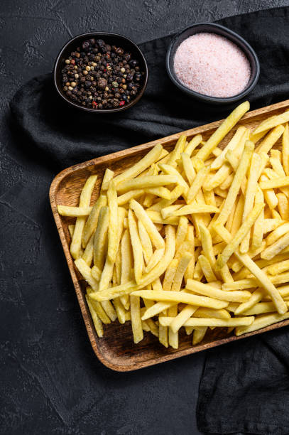 frites français congelées dans un bol en bois. pommes de terre biologiques. fond noir. vue du haut - french fries fast food french fries raw raw potato photos et images de collection