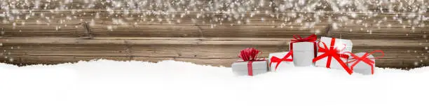 Wide horizontal composition of red ribbon gifts group on wooden background with snowfall. Blank white space for text.