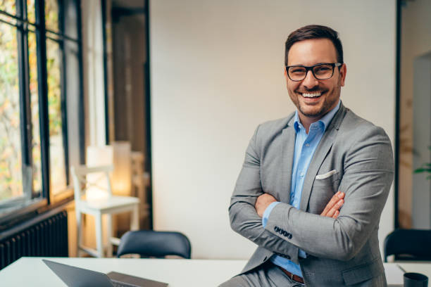 Portrait of young businessman standing in his office with arms crossed Portrait of young happy businessman wearing grey suit and blue shirt standing in his office and smiling with arms crossed facial hair photos stock pictures, royalty-free photos & images