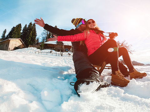 Happy influencers couple having fun with wood vintage sledding on snow high mountains - Young crazy people enoying winter vacation - Travel, love and holiday concept - Focus on faces