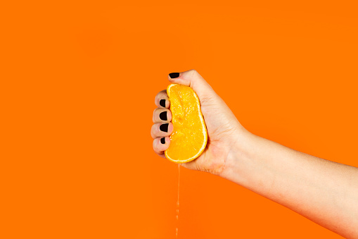Woman crushing a half orange on an orange background