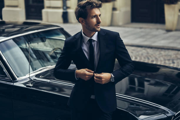 Handsome man in black suit near his old classic car stock photo