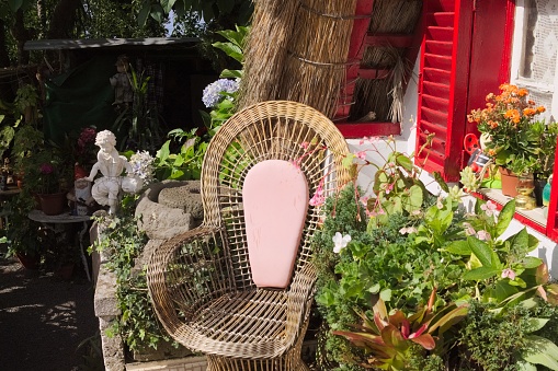 Pink wicker armchair in the garden under a red window near plants and flowers (Madeira, Portugal, Europe)