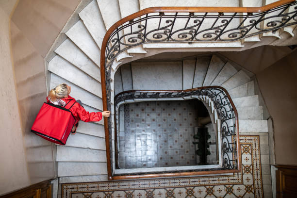 Directly above of delivery woman moving up on stairs Directly above of delivery woman moving up on staircase in residential building, holding container for food on back instant food stock pictures, royalty-free photos & images