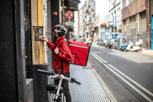 Fast food delivery man with bicycle standing  in front of the door of residential building