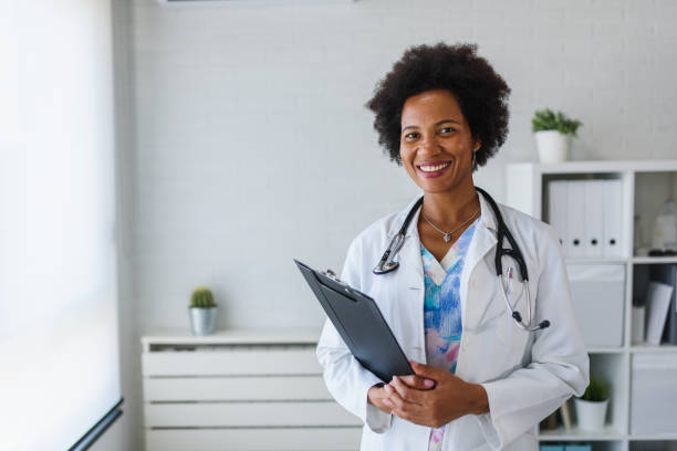 Portrait of female African American doctor standing in her office at clinic Portrait of female African American doctor standing in her office at clinic female doctor stock pictures, royalty-free photos & images