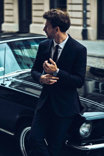 istock Handsome man in black suit near his old classic car 1193307444