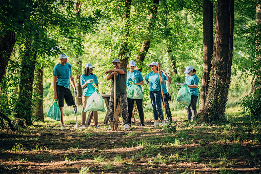 Group of young volunteers and one senior man with blue t-shirts, and caps finished with picking garbage and planting trees at park