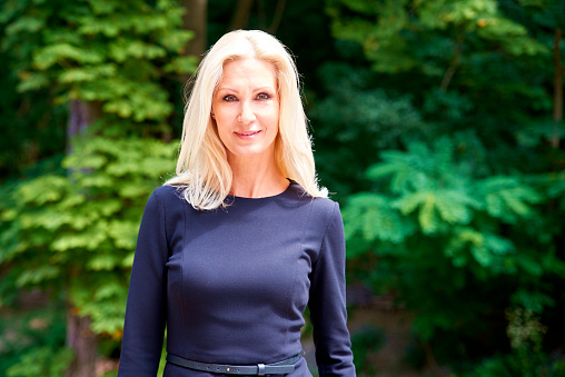 Portrait shot of attractive blond businesswoman wearing black dress while standing outdoor.