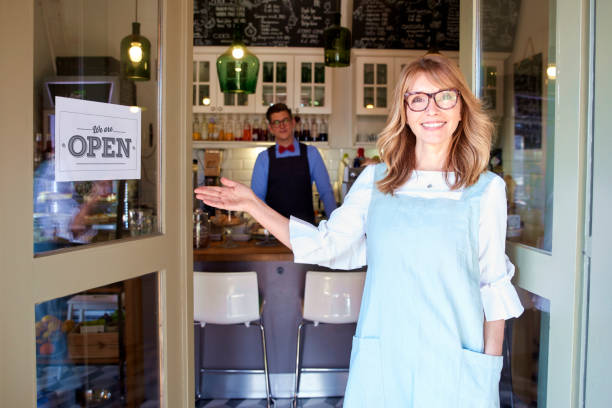 donna proprietaria di piccole imprese in piedi nella porta del caffè e sorridente - small business business owner facade foto e immagini stock