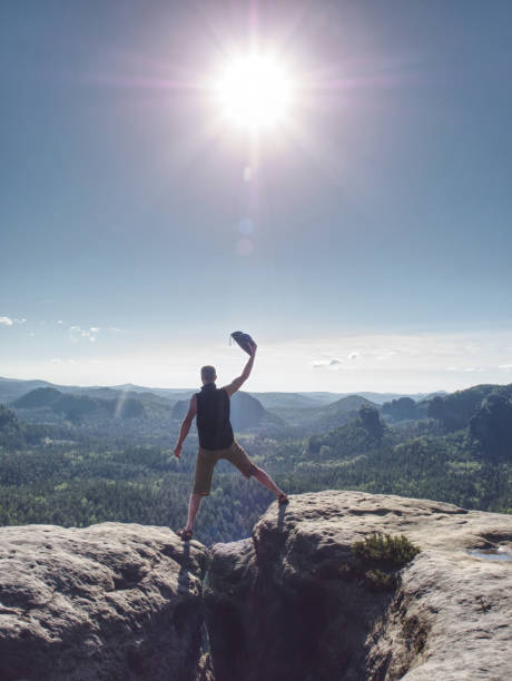 Hiker yelling with happiness on a mountain top. Man on mountain top hiking or climbing. Looking and enjoying inspirational sunshine landscape on rock