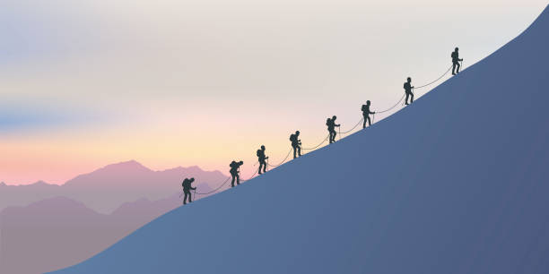 Roped climbers climb the side of a mountain as they walk along a ridge at sunset. A rope of experienced mountaineers climb the snowy slope of a mountain to reach the top. On the horizon the sun sets over the magical landscape. moving up illustrations stock illustrations