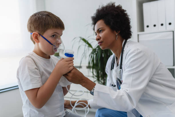 mujer médico afroamericano médico general médico ayudando a niño a poner máscara facial inhalador de nebulizador. tratamiento para el asma para niños. - asthmatic fotografías e imágenes de stock