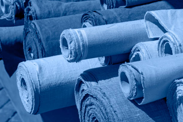 Close up assorted rolls of flax linen fabric and canvas textile on retail market stall, high angle view, blue toned