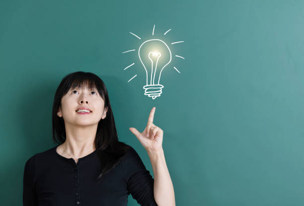 istock Woman pointing light bulb in front of blackboard 1193316718