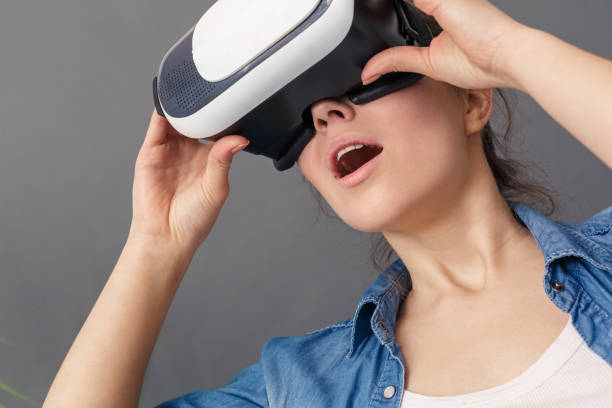 istock Freestyle. Young woman in virtual reality headset sitting studio isolated on greywatching video amaized close-up 1193321859