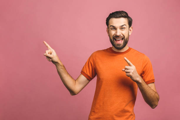 istock Look over there! Happy young handsome man in casual pointing away and smiling while standing against pink background. 1193323344