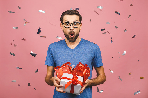 Wonderful gift! Adorable photo of attractive man with beautiful smile holding his birthday present boxes isolated over pink background.