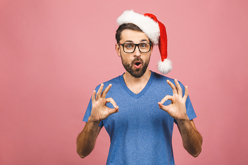 Young handsome man wearing christmas hat over isolated pink background smiling positive doing ok sign with hand and fingers. Successful expression.