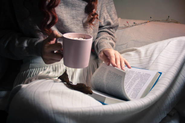 istock Girl drinks cocoa with marshmallow from pink cup and reads book 1193329427