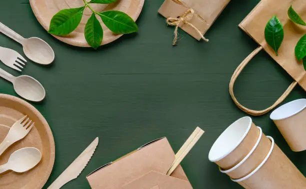 Eco-friendly disposable tableware made of paper on a green wooden table. Wooden spoons, fork, knive, with paper cups, plates, box, bamboo chopstic.