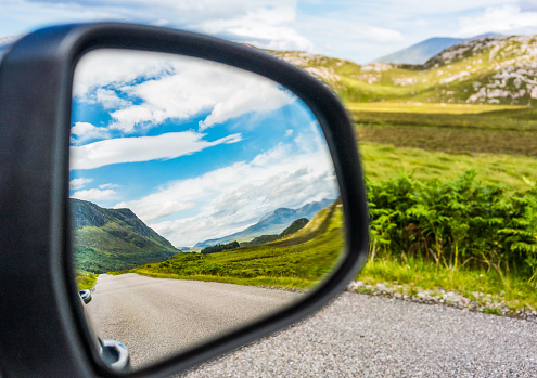 An empty rural road in the far north of Scotland, part of the North Coast 500 route, reflected in the wing mirror of a car.