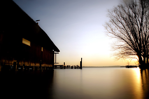 Beautiful tranquil scene. Sunrise / sunset on lake with boathouse and tree