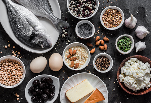 Source of calcium in products - fish, sesame, cheese, cottage cheese, poppy seeds, olives, flax seeds, eggs, legumes, almonds, garlic on a dark background, top view