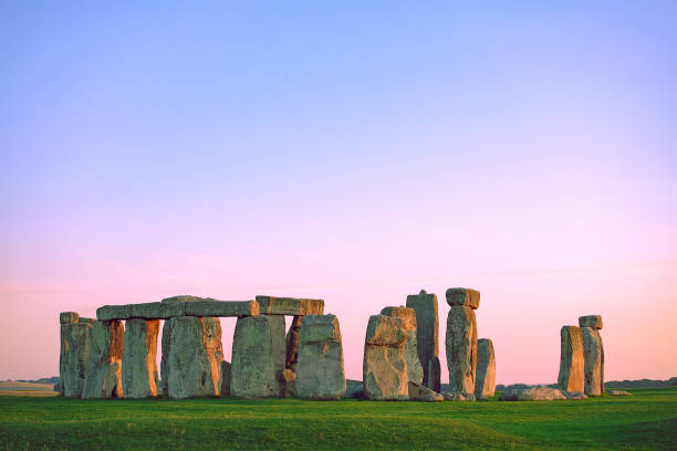 Stonehenge, warm pastel sky, green summer meadow. Prehistoric monument in Wiltshire, United Kingdom. Historic Neolithic Stones. No people. Famous standing stones of Stonehenge in Wiltshire, England. Sunlight, Clear sky, green grass, no people. Colorful, vibrant sunset sky. burial mound photos stock pictures, royalty-free photos & images