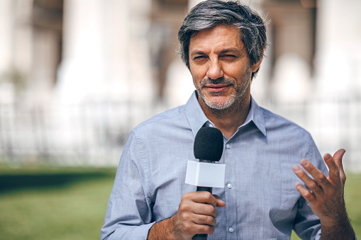 Portrait of Mature gray hair journalist with microphone on the city streets