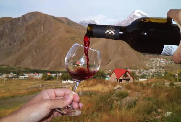 Man's hand pouring red wine from the bottle into wineglass at the village of Mount Kazbek