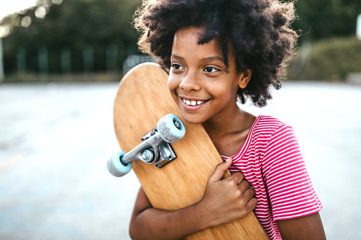 Portrait of adorable pre-adolescent African girl with beautiful smile , holding skateboard outside