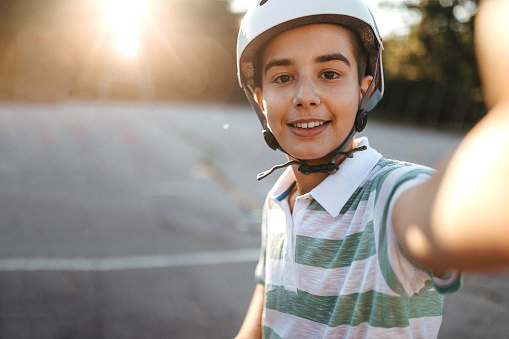 Cute teenage Boy with cycling helmet taking selfie outside on sunny day