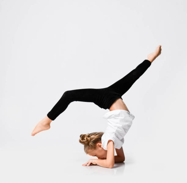 istock Slim athletic kid girl is doing gymnastic acrobatics exercises, stretching with her legs up on white 1193377335