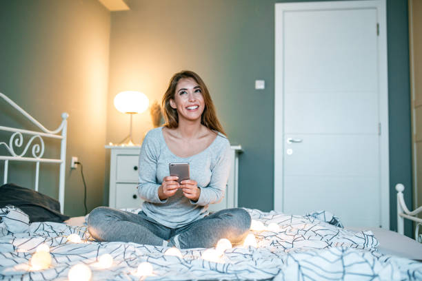 istock Young woman sitting in bed and using smart phone 1193377408