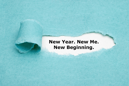 Motivational self encouragement quote New Year, New Me, New Beginning appearing behind torn blue paper.