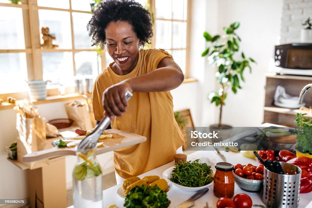 Happy African woman making a lemonade at home Lovely serene African  woman preparing a lemon juice at home in the morning Cooking Stock Photo