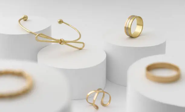 Photo of Modern Golden bow shape bracelet and rings collection on white cylinders platform