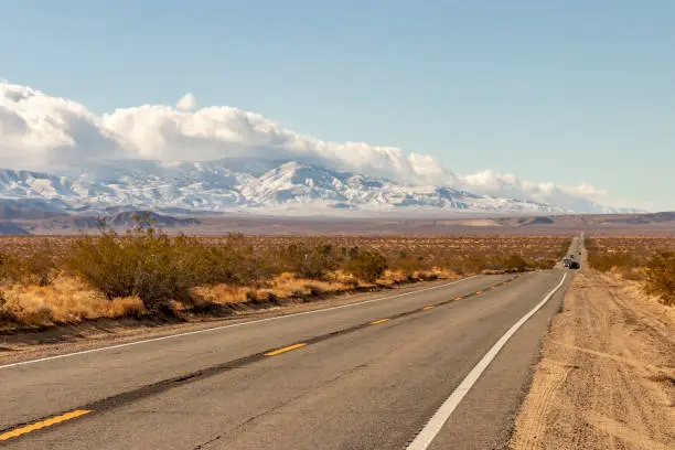 A highway and snowy mountains in late autumn in the Mojave Desert and San Bernardino Mountains, Southern California, USA.