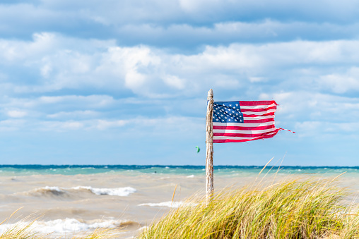 Frankfort, Michigan / USA - October 12 2019: A wind blown, slightly tattered U.S. Flag on an a old wooden flagpole on a Lake Michigan beach.