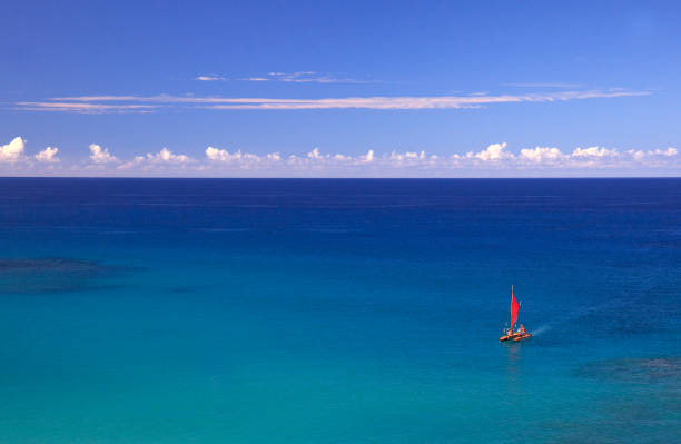 A red sailboat in a stunning turquoise tropical sea. Beautiful baby blue colours in the scene. Image taken on Kona Coast, Big Island, Hawaii.