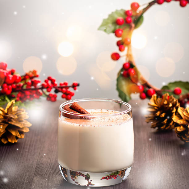 cocktail tradizionale natalizio eggnog con uova, alcol, noce moscata grattugiata e primo piano alla cannella. bevanda tradizionale dolce su tavolo in legno con decorazioni rosse e pigne - luxury milk dinner glass foto e immagini stock