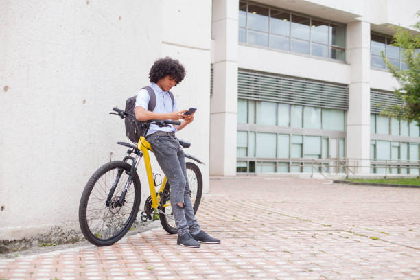 joven de aproximadamente 24 años de edad con su apoyarse en su bicicleta amarilla comprueba su teléfono celular - friendship early teens 13 14 years city street fotografías e imágenes de stock