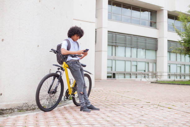 jeune homme d'environ 24 ans avec son penchant sur son vélo jaune vérifie son téléphone cellulaire - friendship early teens 13 14 years city street photos et images de collection