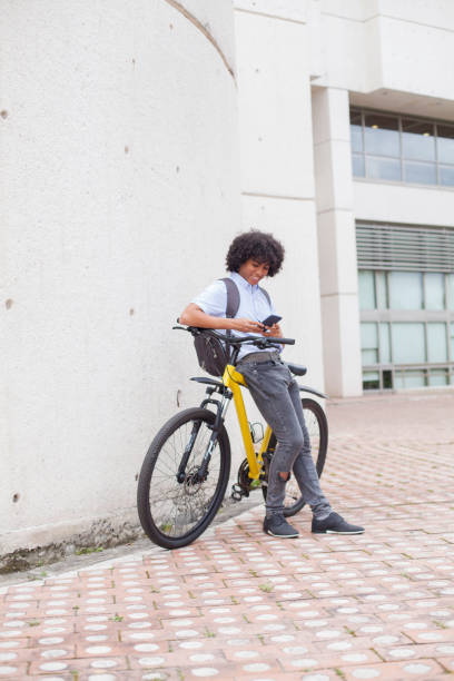 jeune homme d'environ 24 ans avec son penchant sur son vélo jaune vérifie son téléphone cellulaire - friendship early teens 13 14 years city street photos et images de collection