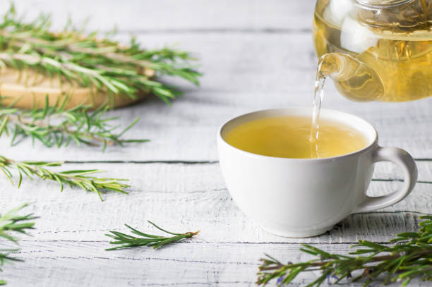 tazza bianca di tè al rosmarino sano versando dalla teiera con mazzo di rosmarino fresco su sfondo rustico in legno bianco, concetto di bevanda calda alle erbe invernale, salvia rosmarinus - herbal tea foto e immagini stock