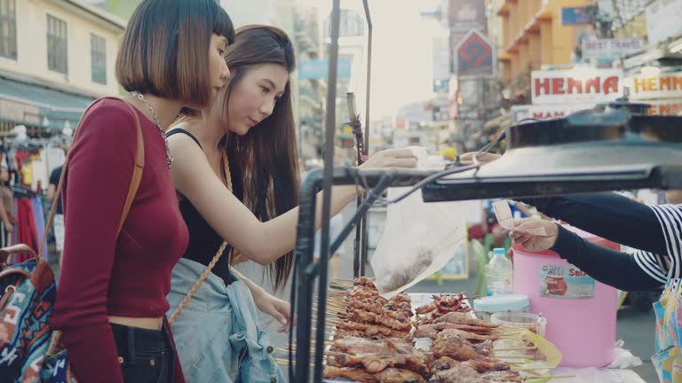 Two Young Women Enjoying Street Food in Khao San Road.