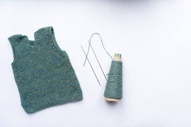 Waistcoat, thread, needles are on white background, view from the top. Knitting concept.